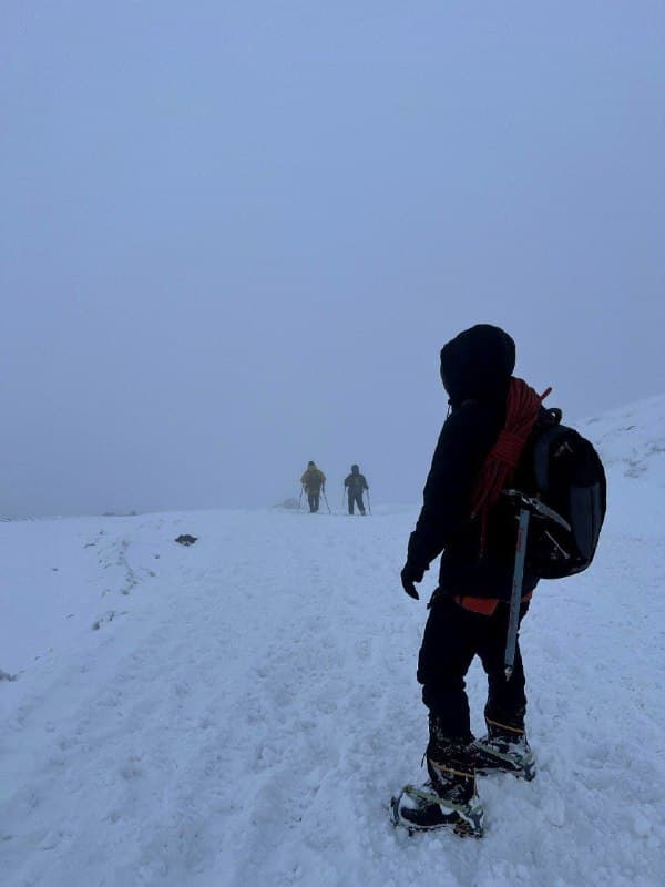 Three trekkers in crampons moving up a snow slope in flat light and low visibility