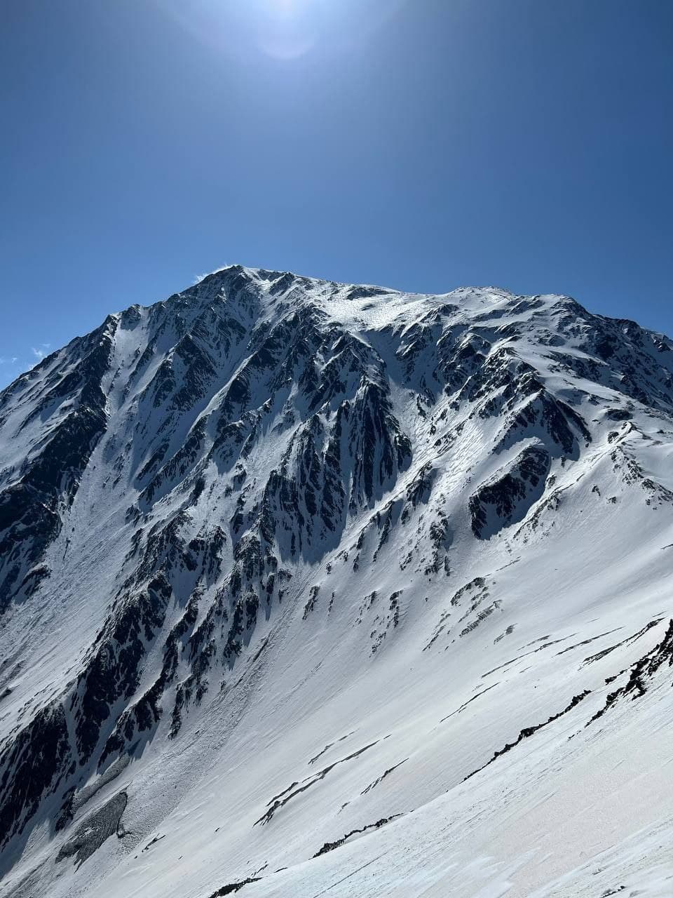 A snow-covered peak with exposed rock ribs, seen against a clear blue sky